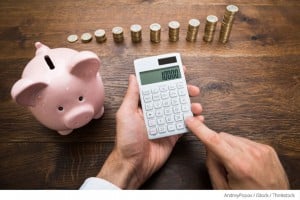 man holding calculator over table with piggy bank and stacked coins
