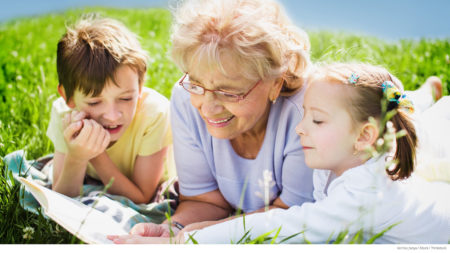 Grandmother with young boy and girl laying in field reading book together