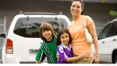 Mom with two young children standing in driveway in front of white SUV
