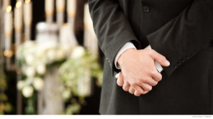 Folded hands at a funeral with candles blurred in background