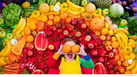 Happy girls laying in rainbow of fruits and vegetables